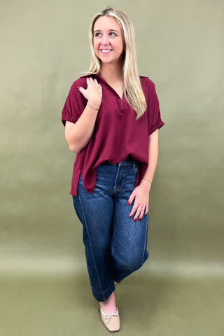 Woman wearing a burgundy top and blue jeans against a green background
