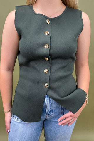 Green sleeveless top with gold buttons worn by a person against a green background
