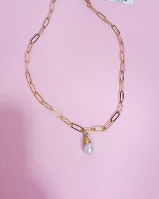 Gold chain necklace with a pearl pendant on a pink background