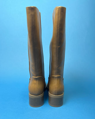 A pair of knee-high taupe faux-leather boots with a low block heel, shown against a solid blue background.