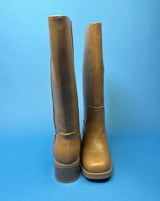 A pair of knee-high taupe faux-leather boots with a low block heel, shown against a solid blue background.
