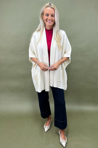 Woman wearing a white cardigan, red top, and dark pants on a green background