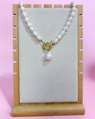 Pearl necklace with a gold clasp on a display stand against a pink background