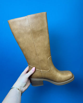 A pair of knee-high taupe faux-leather boots with a low block heel, shown against a solid blue background.