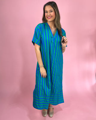 Woman wearing a blue and green striped dress against a pink background
