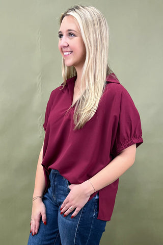 Woman wearing a burgundy shirt and blue jeans against a green background