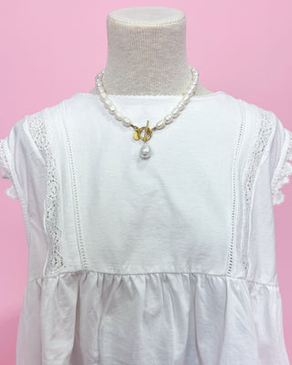 White lace-trimmed dress on a mannequin with a pink background
