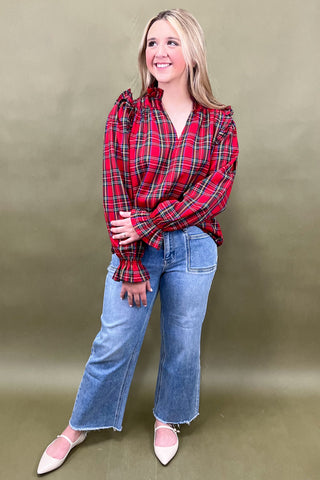 Woman wearing a red plaid shirt and blue jeans against a beige background