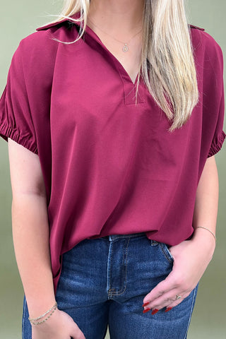 Person wearing a maroon top and blue jeans against a green background
