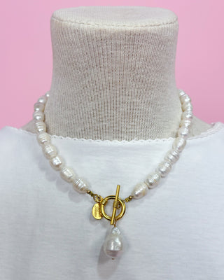 Pearl necklace with a gold clasp on a mannequin against a pink background