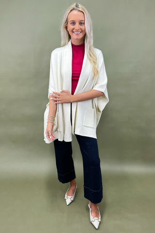 Woman wearing a white cardigan, red top, and dark pants on a green background