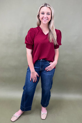 Woman wearing a red blouse and blue jeans against a plain background