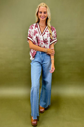 Woman wearing a floral blouse and blue jeans against a green background