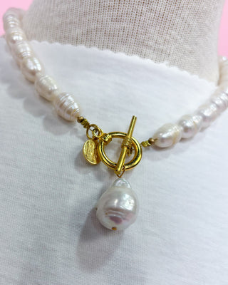 Pearl necklace with a gold clasp on a mannequin bust.
