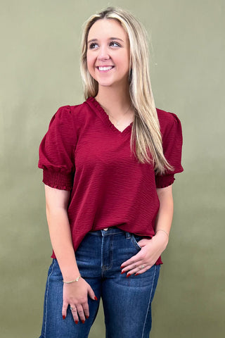 Woman wearing a red blouse and blue jeans against a green background
