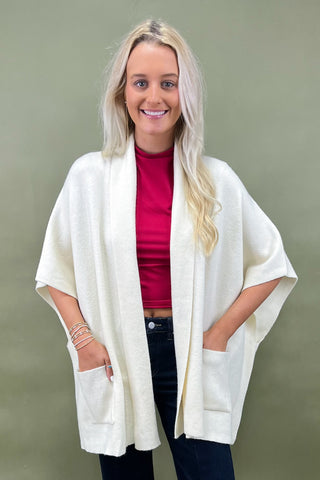 Woman wearing a white cardigan, red top, and dark pants on a green background