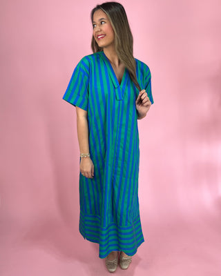 Woman wearing a blue and green striped dress against a pink background