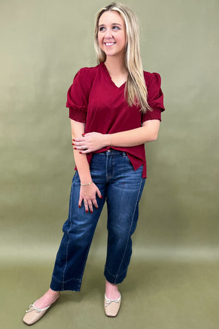 Woman wearing a red blouse and blue jeans against a green background