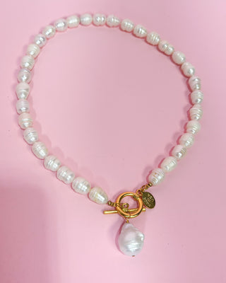 Pearl necklace with a gold clasp on a pink background