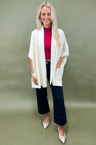 Woman wearing a white cardigan, red top, and dark pants on a green background