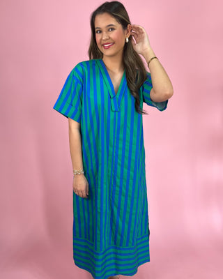 Woman wearing a blue and green striped dress against a pink background