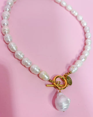 Pearl necklace with a gold clasp and pendant on a pink background