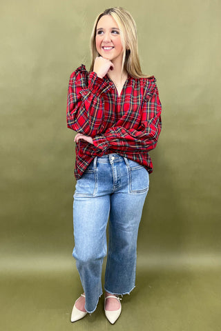 Woman wearing a red plaid shirt and blue jeans against a green background