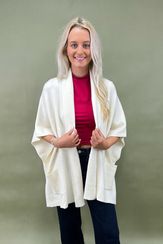 Woman wearing a white cardigan over a red top and black pants on a green background