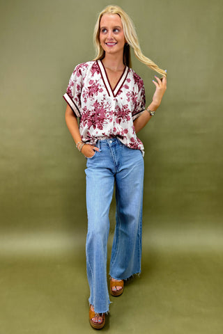 Woman wearing a floral blouse and blue jeans against a green background