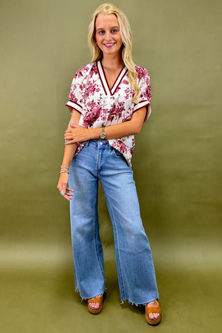 Woman wearing a floral blouse and blue jeans against a green background