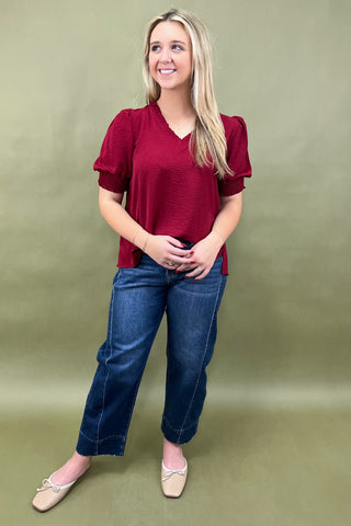 Woman wearing a red blouse and blue jeans against a green background