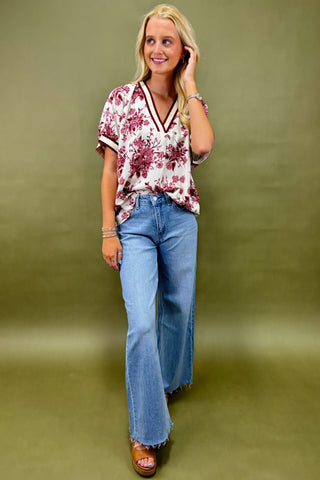 Woman wearing a floral top and blue jeans against a green background