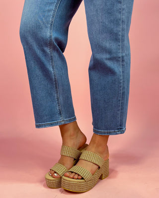 Gold platform sandals worn with blue jeans on a pink background