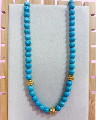 Turquoise beaded necklace with gold accents on a light gray surface