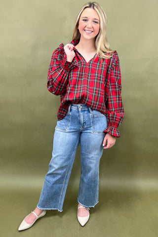 Woman wearing a red plaid shirt and blue jeans against a green background