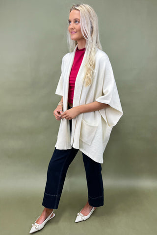 Woman wearing a white cardigan, red top, and dark pants on a green background
