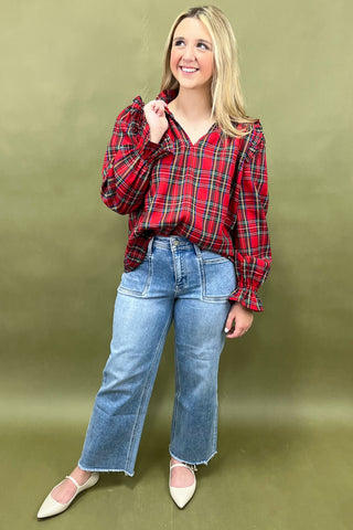 Woman wearing a red plaid shirt and blue jeans against a green background