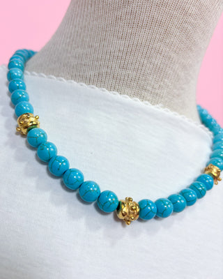 Turquoise beaded necklace with gold accents on a white fabric background
