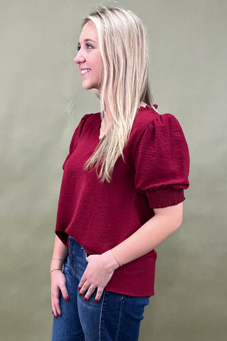 Woman wearing a red blouse with puff sleeves against a plain background