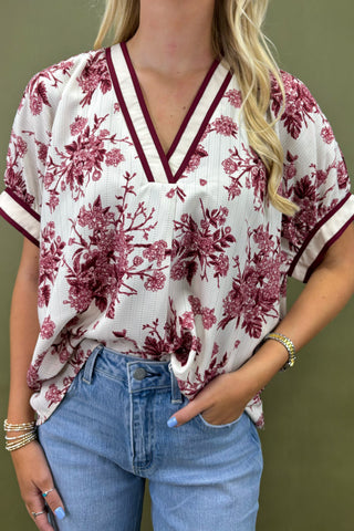 Woman wearing a white blouse with red floral pattern and blue jeans against a green background