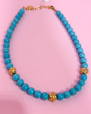 Turquoise beaded necklace with gold accents on a pink background