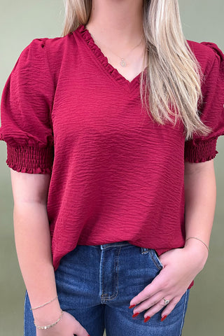 Person wearing a red blouse with puff sleeves and blue jeans against a green background