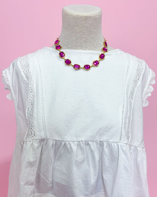White dress with a pink and gold necklace on a mannequin against a pink background