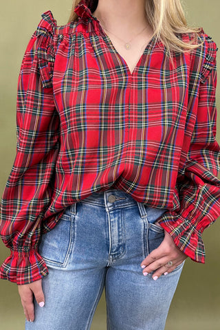 Red plaid blouse with ruffled sleeves worn by a person against a green background