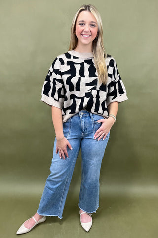 Woman wearing a black and white patterned top and blue jeans against a green background