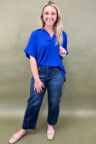 Woman wearing a blue top and jeans against a plain background