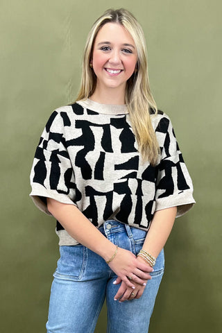 Woman wearing a black and white patterned top with blue jeans against a green background
