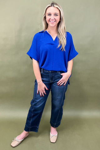 Woman wearing a blue top and jeans against a green background