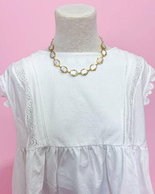 White dress with gold necklace on a mannequin against a pink background