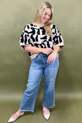 Woman wearing a black and white patterned top and blue jeans against a green background